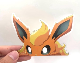 May include: A die-cut sticker depicting the Pokémon character Flareon. The sticker is predominantly orange and yellow, with large eyes and pointed ears. The character is shown peeking over an edge, creating a playful and engaging design.
