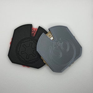 May include: Two 3D printed keychains, one black with the Star Wars Imperial symbol and the other gray with the Rebel Alliance symbol.