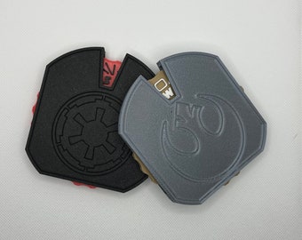 May include: Two 3D printed keychains, one black with the Star Wars Imperial symbol and the other gray with the Rebel Alliance symbol.
