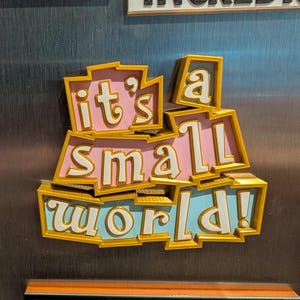 May include: A pink and blue 3D magnet with the words "it's a small world!" in gold lettering.
