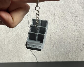 May include: A gray plastic keychain shaped like a ride vehicle from a popular theme park attraction. The keychain has four seats and a silver chain.