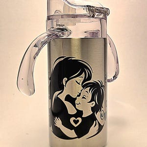 May include: Stainless steel water bottle with a clear plastic lid and handles. The bottle features a black and white graphic of a mother and child embracing, with a heart symbol. The design is centered on the bottle.