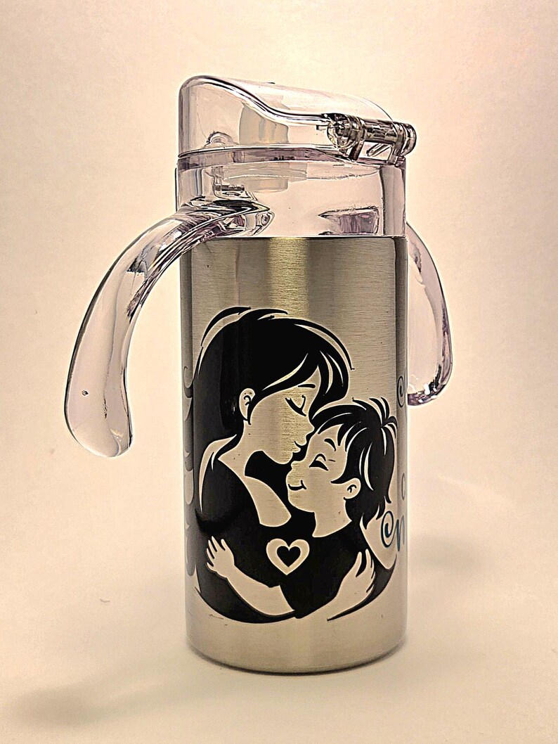 May include: Stainless steel water bottle with a clear plastic lid and handles. The bottle features a black and white graphic of a mother and child embracing, with a heart symbol. The design is centered on the bottle.