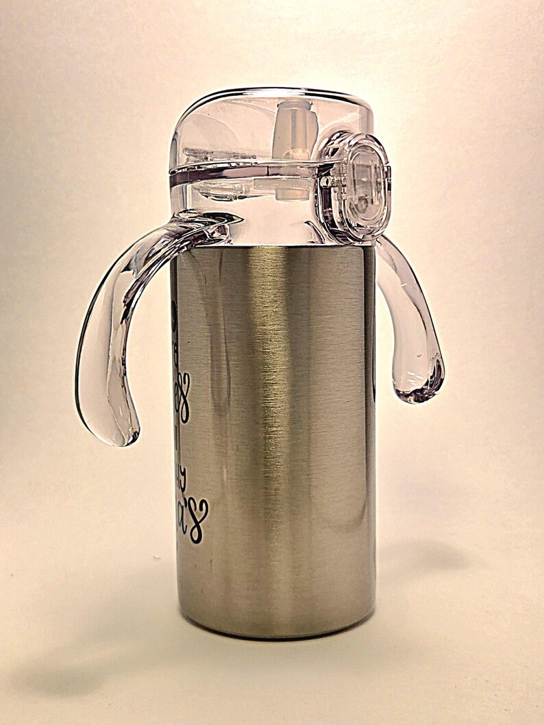 May include: Stainless steel sippy cup with a clear plastic lid, handles, and straw. The cup has a brushed metal finish and features black cursive text. The lid has a flip-top closure for easy access.
