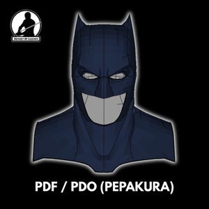 Op de afbeelding: Illustratie van een donkerblauw Batman-masker met een brede, grijnzende grijns. De afbeelding bevat de tekst "PDF / PDO (PEPAKURA)" onderaan en een logo in de linkerbovenhoek. Het masker heeft puntige oren en een gestileerd ontwerp.