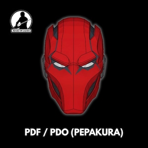 Puede incluir: Diseño de casco rojo con una apariencia estilizada y angular. El casco presenta una zona de visera prominente con aberturas para los ojos blancas y detalles en gris oscuro. El texto "PDF / PDO (PEPAKURA)" está en la parte inferior, con un logo en la esquina superior izquierda.