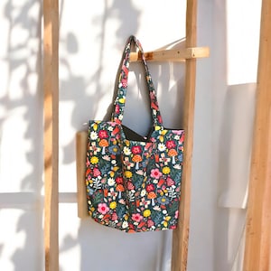 May include: A green tote bag with a colorful floral and mushroom print. The bag has two black straps.