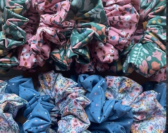 May include: A collection of colorful fabric scrunchies with floral patterns. The scrunchies are in shades of pink, green, blue, and white.