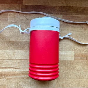 May include: A red insulated water bottle with a white lid and a white strap. The bottle has a cylindrical shape with a ridged bottom. The strap is attached to the bottle with white loops.