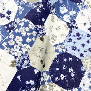 May include: Close-up of a fabric with a patchwork design. The fabric features a variety of blue hues, including navy, light blue, and white, with floral patterns. The design is composed of hexagonal shapes, creating a quilt-like appearance.
