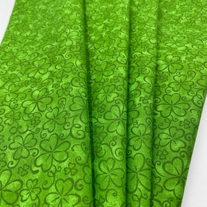 May include: Green fabric with a repeating pattern of four-leaf clovers and swirls.