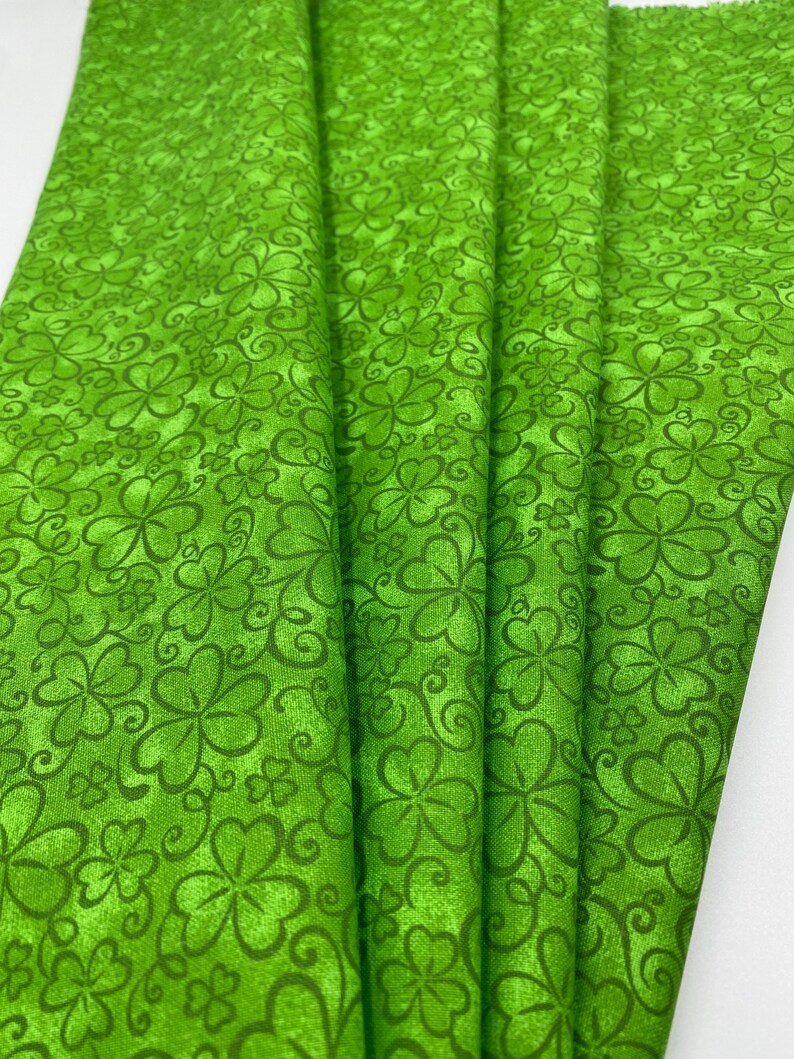 May include: Green fabric with a repeating pattern of four-leaf clovers and swirls.