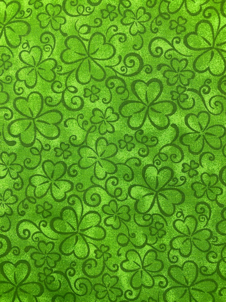 May include: Green fabric with a repeating pattern of shamrocks and swirls.