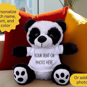 May include: A plush panda bear with black and white fur, wearing a white t-shirt. The shirt has the text "YOUR TEXT OR PHOTO HERE". The bear is sitting in front of red and yellow pillows. Text on the image says "Personalize with name, font, and color" and "Or add a photo".
