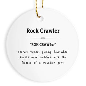May include: Round white ceramic ornament with the text "Rock Crawler" and a definition. The ornament has a gold string for hanging. The text includes the pronunciation "ROK CRAW-lur" and a description of rock crawling.