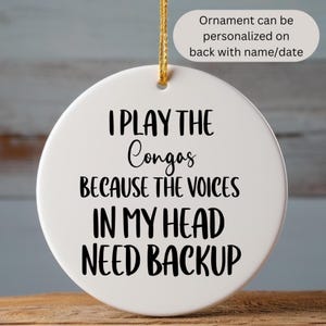 May include: White ceramic ornament with black text that reads "I play the Congas because the voices in my head need backup".