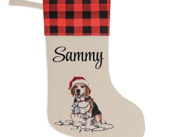 May include: A beige Christmas stocking featuring a red and black buffalo plaid cuff at the top. The name Sammy is printed in black script. Below the name is an illustration of a beagle dog wearing a Santa hat and tangled in Christmas lights.