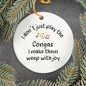 May include: White round Christmas bauble with black text that reads "I don't just play the Congas I make them weep with joy". There are musical notes above the word "Congas".
