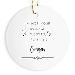 May include: A white ceramic disc ornament with a gold hanging loop. The text "I'M NOT YOUR AVERAGE MUSICIAN, I PLAY THE Congas" is printed in black, with musical notes as decoration.