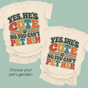 May include: Two cream-colored t-shirts with retro-style graphic text. One shirt reads: YES, HE'S CUTE NO, YOU CAN'T PET HIM. The other reads: YES, SHE'S CUTE NO, YOU CAN'T PET HER. Both feature a small paw print icon and colorful, distressed lettering.