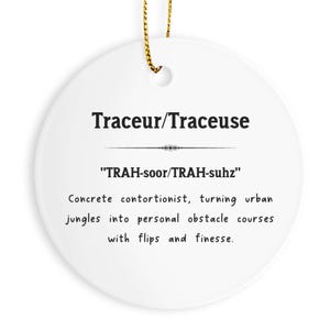 May include: A white ceramic ornament with the text "Traceur/Traceuse" in black. Below the text is the phonetic pronunciation "TRAH-soor/TRAH-suhz". The ornament describes a concrete contortionist turning urban jungles into obstacle courses.