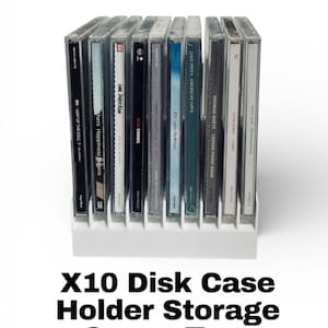 May include: A white plastic X10 disk case holder with a row of CD cases. The CD cases are clear with various album covers and text. The text "X10 Disk Case Holder Storage Space Tray" is below the holder.