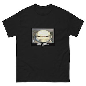 May include: Black t-shirt featuring a meme graphic. The graphic is a close-up of a face wrapped in bandages, with the text "JOTCHUA" and "graham" below. The t-shirt is made of a soft, comfortable material.
