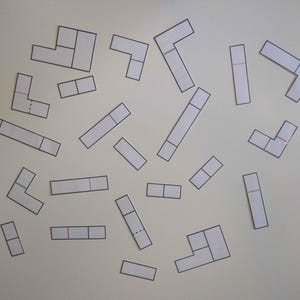 Puede incluir: Una colecci&oacute;n de 20 piezas de rompecabezas en forma de L de papel blanco, cada una con una configuraci&oacute;n diferente de l&iacute;neas y cuadrados. Las piezas est&aacute;n dispersas sobre un fondo blanco.
