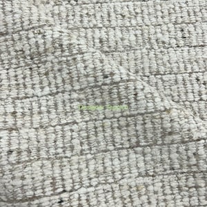 Puede incluir: Primer plano de una alfombra texturizada blanca y beige con un patrón tejido. La alfombra tiene una textura suave y esponjosa.