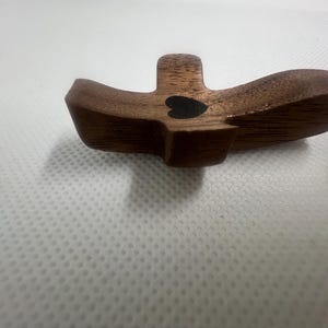 May include: A wooden cross with a black heart in the center. The cross is made of dark wood and has a smooth finish.
