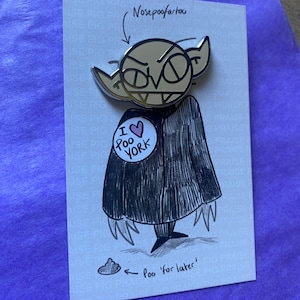 Puede incluir: Pin con un diseño de vampiro de dibujos animados, que incluye el texto "I love York" en un botón. El pin tiene una capa negra y el texto "Poo 'for later'" con un dibujo de un montón de caca.