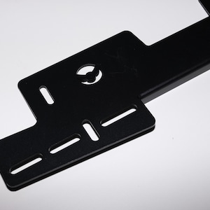 May include: A black metal bracket with multiple rectangular and circular cutouts. The bracket has a flat, angular design with a series of evenly spaced slots and a central circular opening. The object is set against a white background.