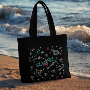 May include: Black tote bag with a colourful graphic design featuring the words "Space Boujee" and retro space-themed illustrations.