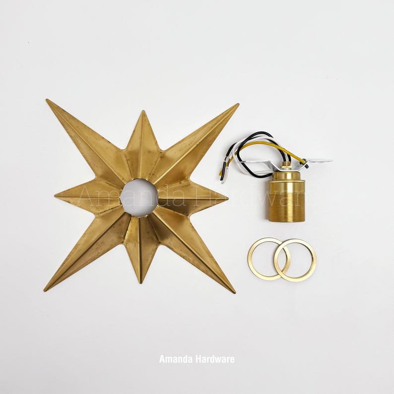 May include: A gold-toned star-shaped metal light fixture component with a central circular opening, accompanied by a brass-colored cylindrical light socket with attached black, white, and yellow wires, and two matching circular metal rings.