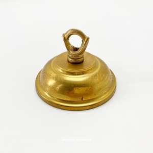 May include: A brass ceiling rose with a loop for suspension. The rose is a warm gold colour and has a rounded shape. The text "Amanda Hardware" is at the bottom.