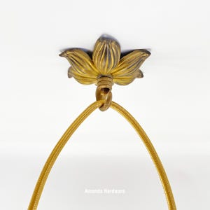 Op de afbeelding: Gouden metalen plafondarmatuur met een decoratief bloemmotief. De armatuur is bevestigd aan een gouden snoer.