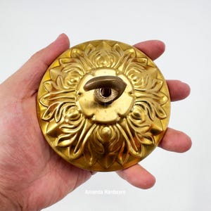 May include: A gold-colored, ornate door knob with a floral design. The knob has a central keyhole and a curved handle. The text "Amanda Hardware" is visible at the bottom.