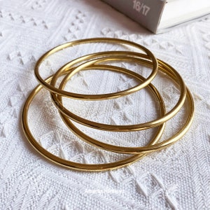 May include: Four gold-colored metal bangles stacked on top of each other. The bangles are smooth and shiny.