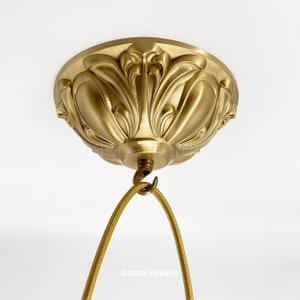 May include: A gold ceiling fixture with a decorative, ornate design. The fixture has a hook for hanging a light fixture.