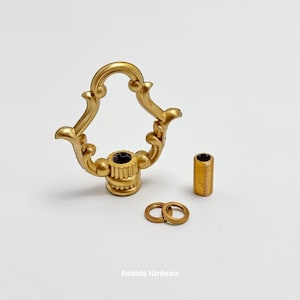 May include: A collection of gold-colored hardware components, including a decorative handle with an ornate design, a cylindrical piece, and two small circular washers. The components are likely for furniture or decorative purposes.