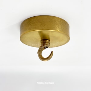 May include: A brass ceiling hook with a round base and a curved hook. The hook is designed for hanging light fixtures.