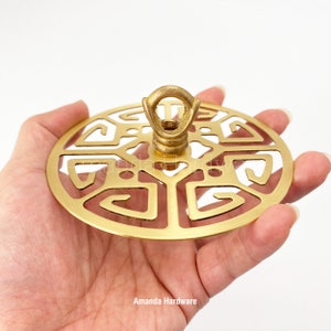 May include: A gold metal ceiling canopy with a decorative geometric design and a hanging loop. The canopy is designed for use with a light fixture.