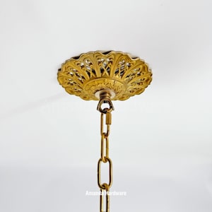 Puede incluir: Rosetón de techo dorado ornamentado con un diseño de filigrana decorativo. Una cadena dorada a juego cuelga debajo, sujeta al rosetón. El texto "Amanda Hardware" es visible en la parte inferior.
