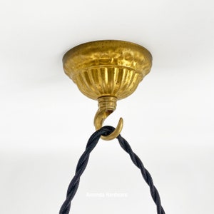 May include: A gold ceiling fixture with a decorative, fluted canopy and a hook for hanging a light fixture. A black electrical cord is attached to the hook.