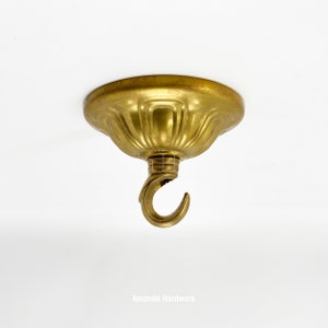 May include: A gold ceiling canopy with a decorative fluted design and a hook for hanging a light fixture.