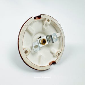 May include: A white ceramic light fixture base with a brown rim. The base has a metal bracket and a gold-colored center. The fixture has three screw holes and a small notch. The text "Amanda Hardware" is at the bottom.