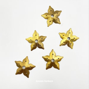 May include: Five gold metal flower-shaped decorative pieces with a hole in the center. Each piece has six points and a slightly textured surface.