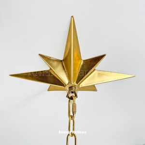 May include: A gold-colored, star-shaped ceiling light fixture. The fixture has eight points and is suspended by a gold chain. The text "Amanda Hardware" is visible on the fixture.