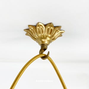 May include: Gold ceiling fixture with a decorative flower-shaped canopy and a hook for hanging a light fixture.