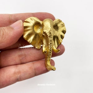 Puede incluir: Una figurita de cabeza de elefante de color dorado con una superficie texturizada. La figurita es una pieza decorativa y está hecha de metal.